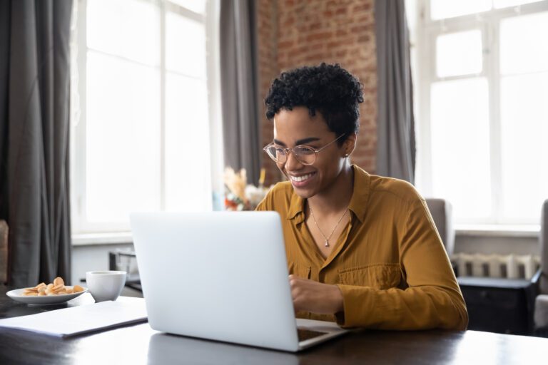 Happy young African American woman working on computer at home.